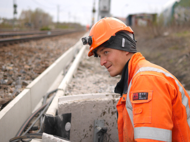 En Seko-medlem i brandgul jacka och hjälm invid ett järnvägsspår.