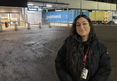 Bild på Maryam, förtroendevald i Seko, stående framför Växjö paketterminal, i bakgrunden syns även flera PostNord-lastbilar.