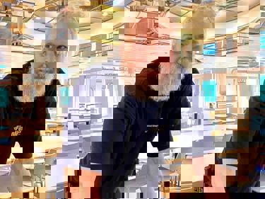 Man med vitt skägg och arbetskläder lutar sig över ett bord i en konferenslokal.