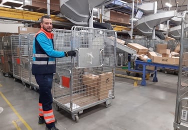 TErminalarbetare i PostNorduniform drar en paketbur inne på en terminal.