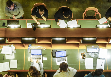 Personer som sitter och studerar vid ett bord i kungliga biblioteket med av datorer och böcker.