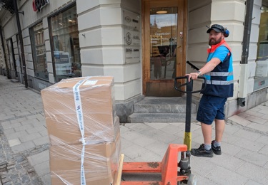 En chaufför på trottoar levererar gods med handtruck.