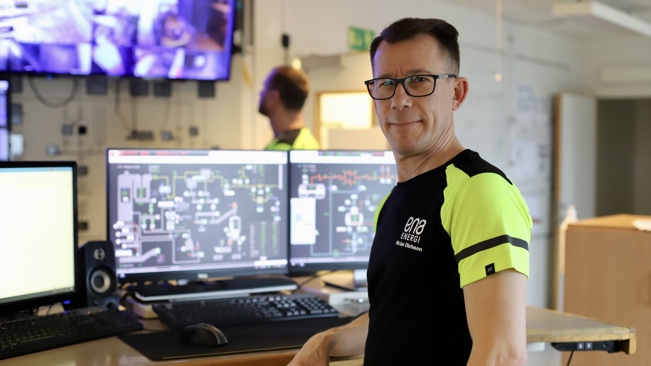Seko-medlem inom energi på sin arbetsplats, nöjt leende framför en datorskärm.