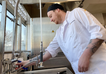 En manlig kock i vita kockkläder som sätter på kranen i köket