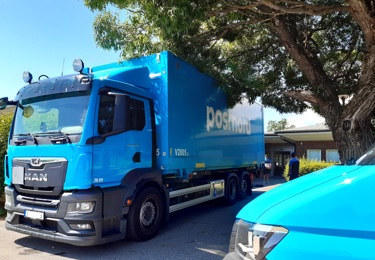 En PostNord-lastbil parkerad under en grönskande träd.