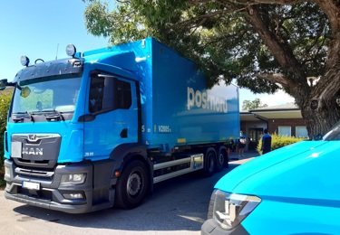 En PostNord-lastbil och fronten av en PostNord-skåpbil med ett träd i bakgrunden