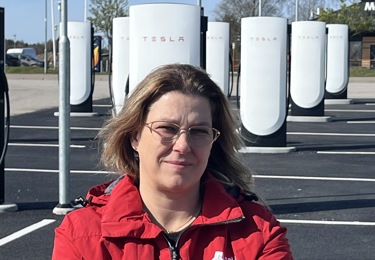 Sekos avtalssekreterare Ulrika Nilsson iklädd röd jacka med armarna i kors framför en Tesla-laddstation.