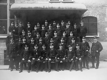 Ett trettiotal brevbärare i uniform uppställda framför Postkontoret Stockholm 1909.