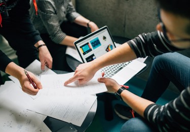 Tre personer runt ett lågt bord med en dator och papper på